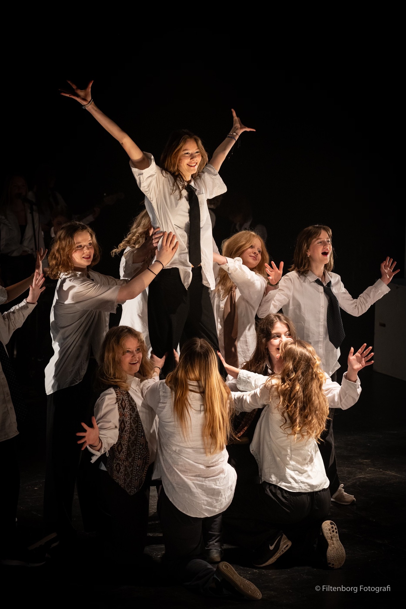 Efterskoleelever i fuld gang på scenen. Alle iført skjorte og slips.